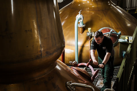 Person working on a large copper still in a distillery